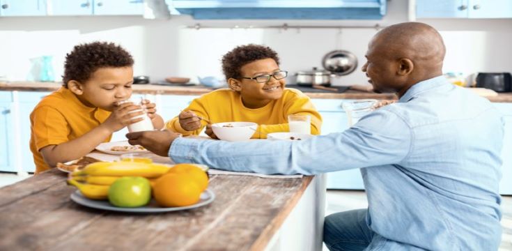 gentle-care-charming-young-father-giving-his-son-glass-milk-helping-him-drink-while-they-all-sitting-together-table-eating-breakfast