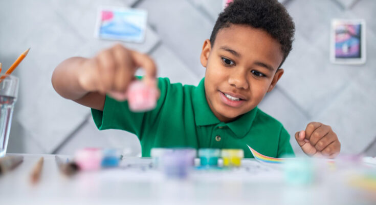 boy-sitting-table-looking-paints-with-enthusiasm