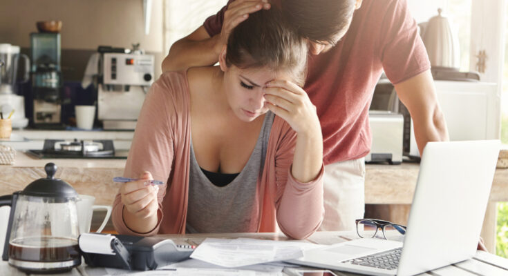unhappy-couple-unable-pay-loan-time-stressed-female-doing-paperwork-sitting-table-with-laptop-papers-calculator-cell-phone-man-trying-support-his-wife